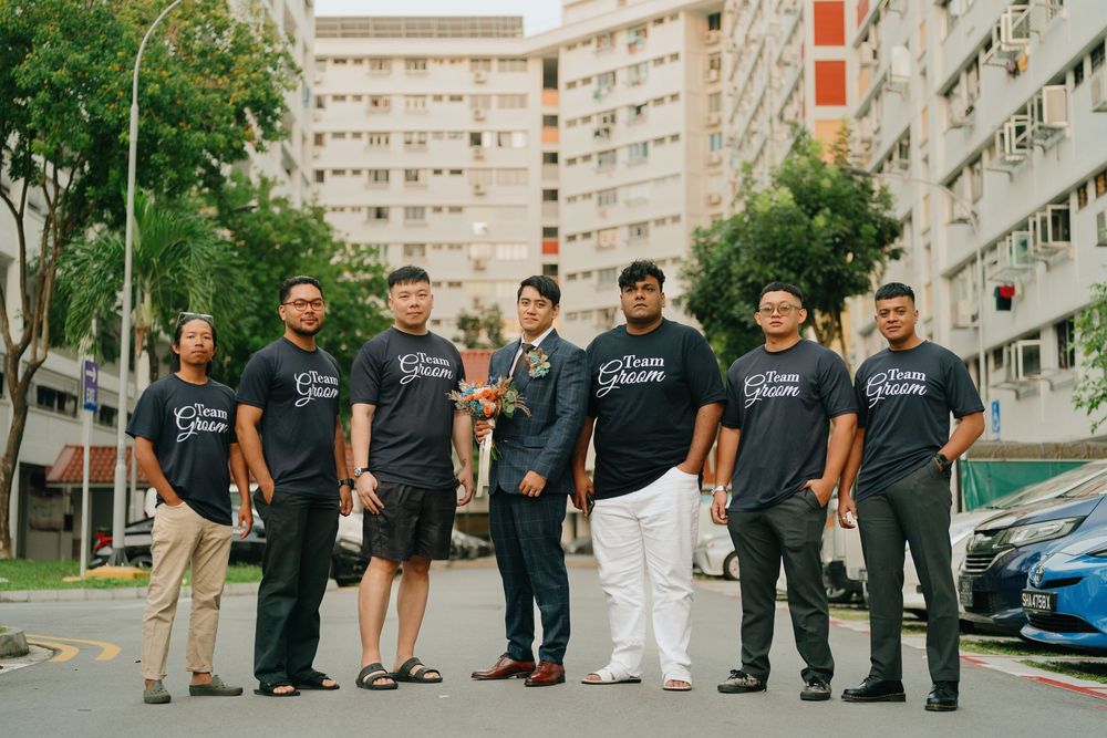 A group of people wearing matching dark t-shirts pose together outside residential apartment buildings.