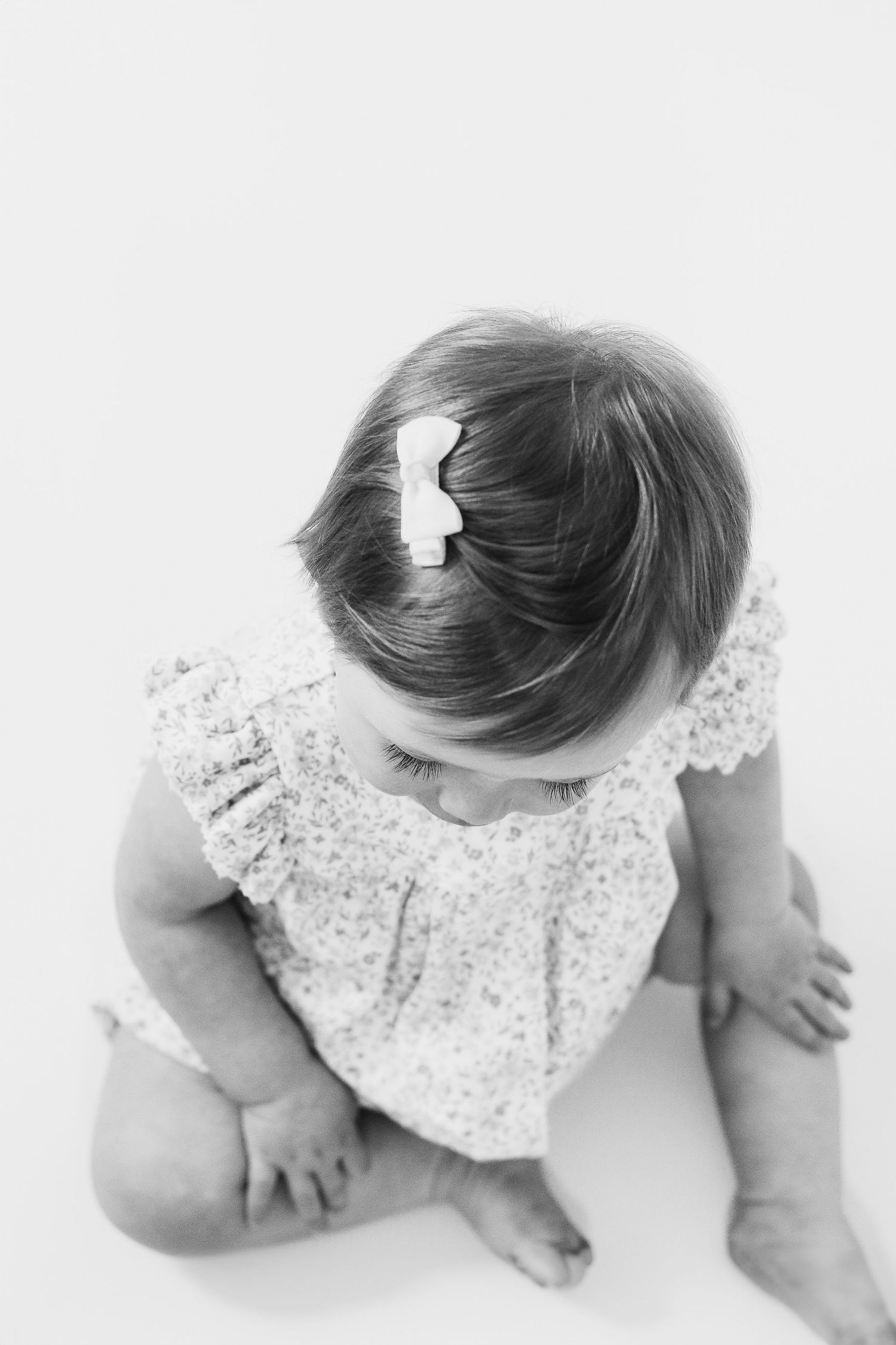 Black and white artistic photo of a baby in a white lace dress exploring against a light background, during birthday shoot in Nottingham