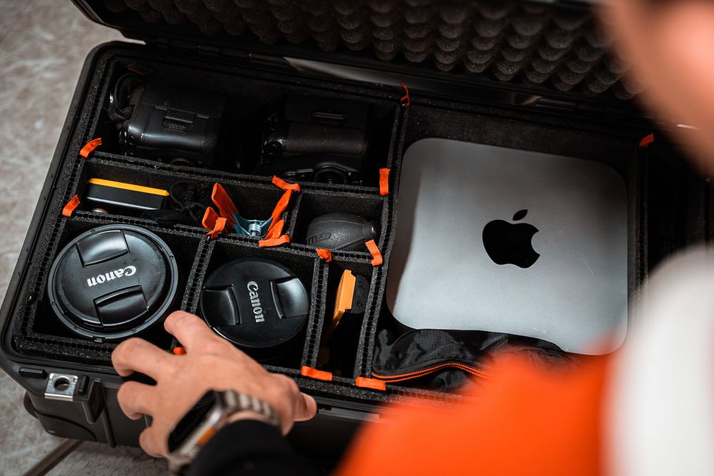 Hand opening a black protective hardshell camera equipment case with orange lining on dark surface.