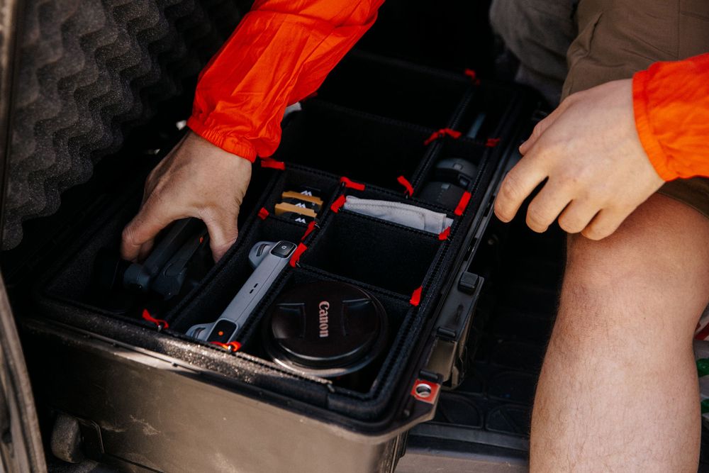 Two hands wearing bright orange safety gloves performing automotive maintenance tasks under the hood.