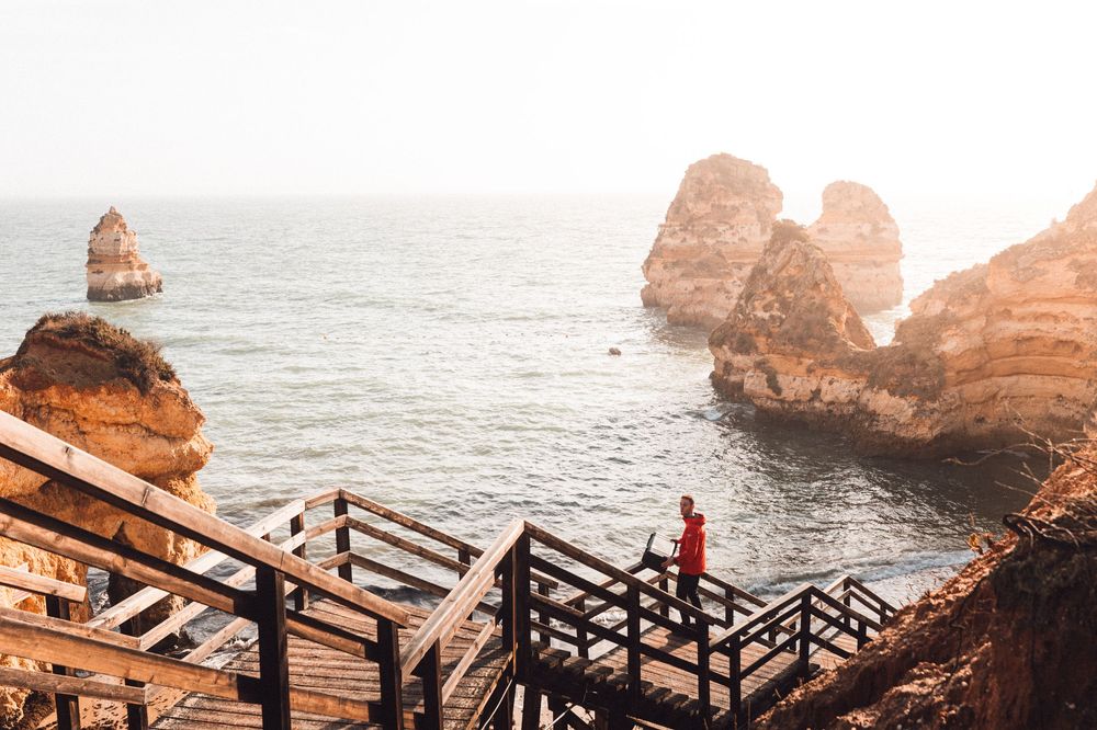 Wooden stairs lead down to a scenic viewpoint overlooking rugged coastal rock formations and ocean waves.