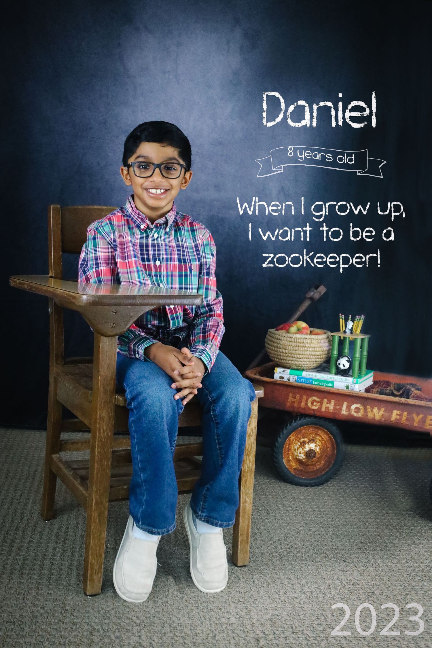 Young student sitting on wooden bench against chalkboard wearing plaid shirt and glasses for school photo session.