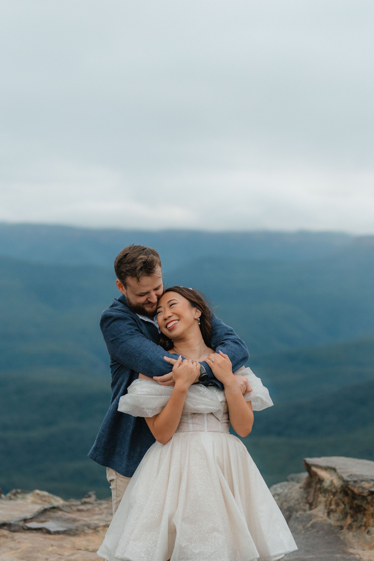 A joyful embrace captured against a misty mountain backdrop during sunset.
