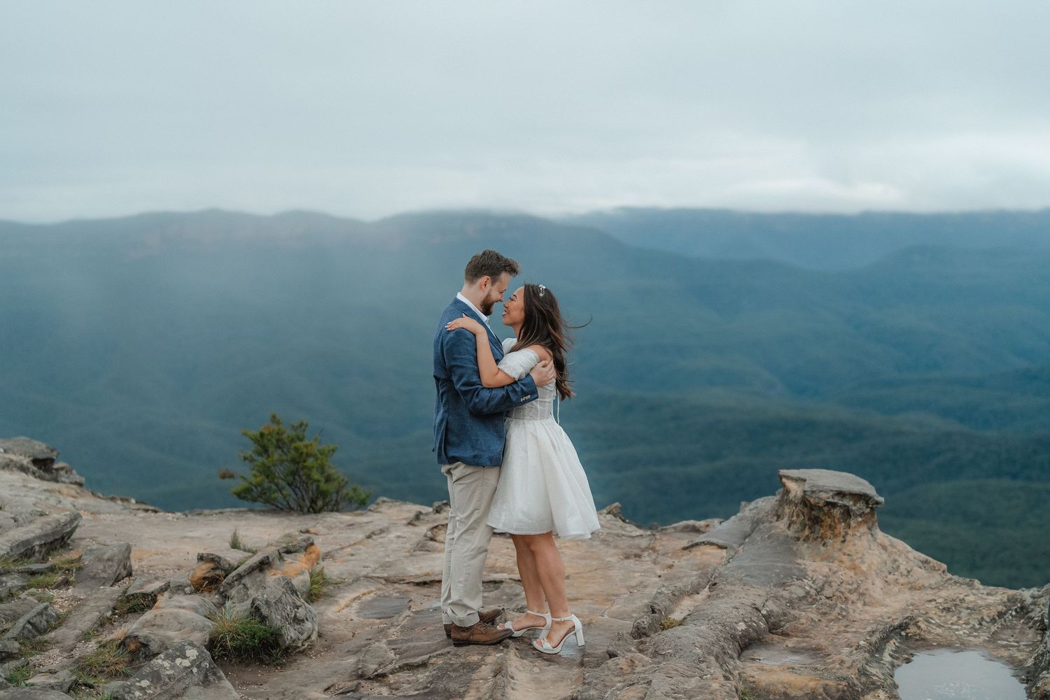 Intimate moment captured between couple on rocky mountain overlook during cloudy afternoon.
