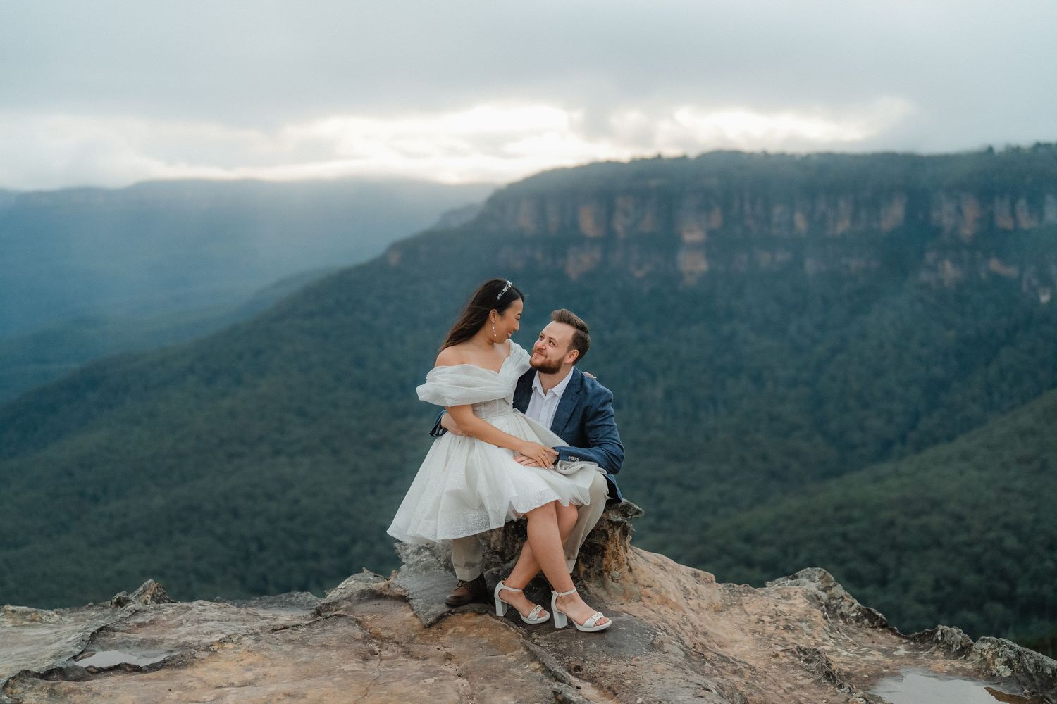 Couple sitting together on a rocky cliff edge overlooking the Blue Mountains valley.