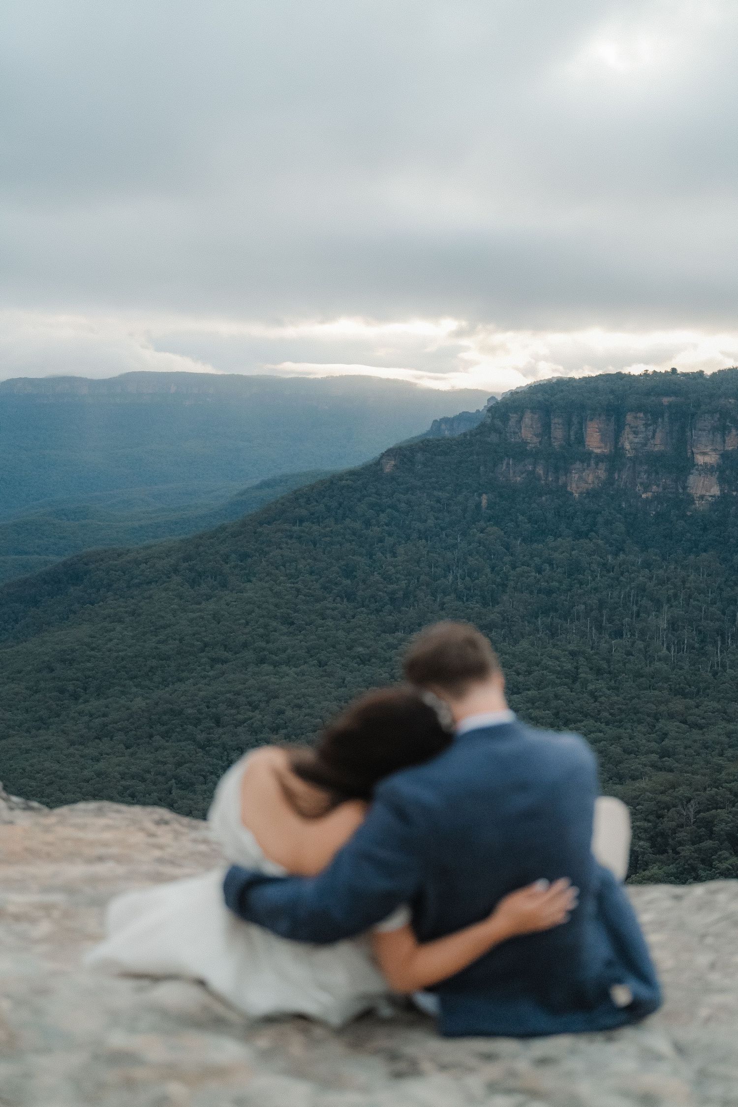 Pair relaxes together on mountain cliff edge while taking in panoramic valley views below.