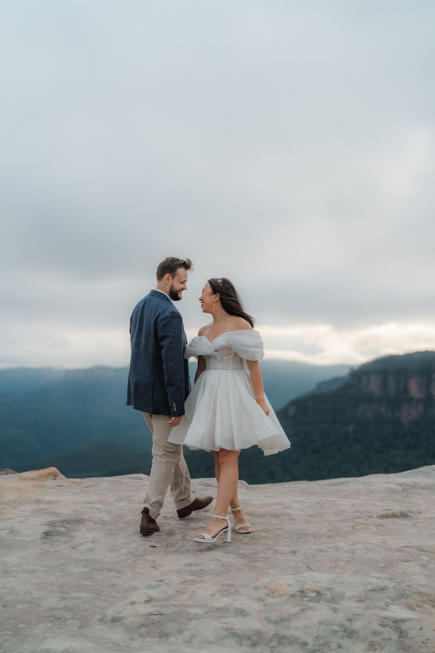 Couple explores rocky mountain overlook with dramatic cloudy skies and valley views.