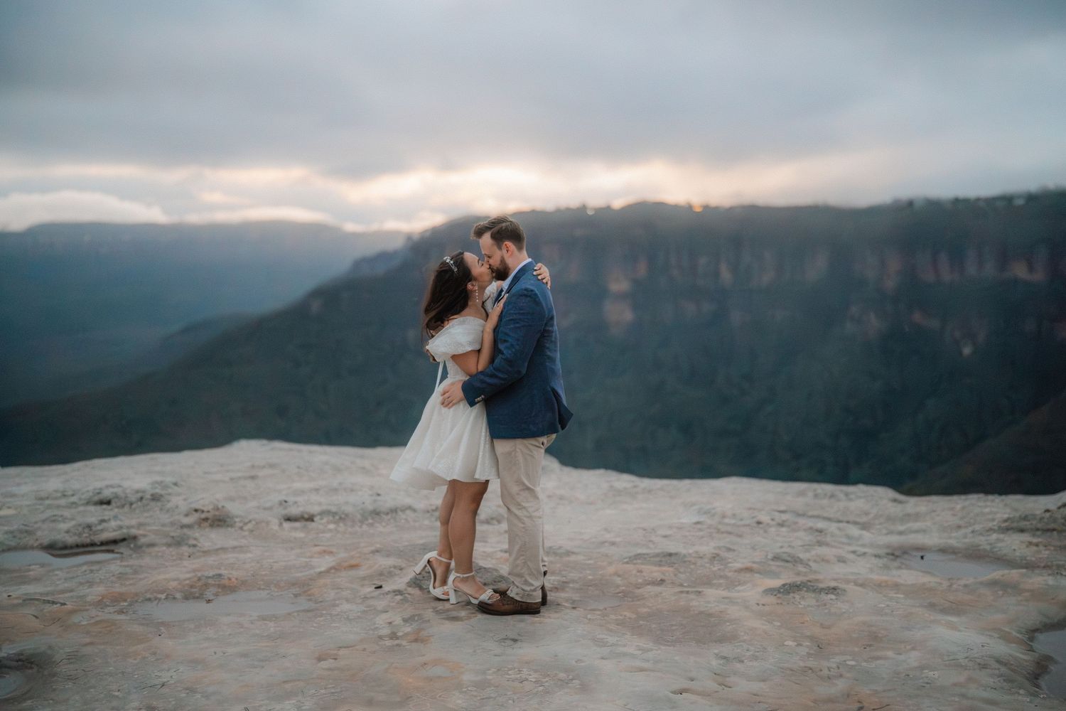 Intimate moment captured between couple on mountain precipice with valley views.