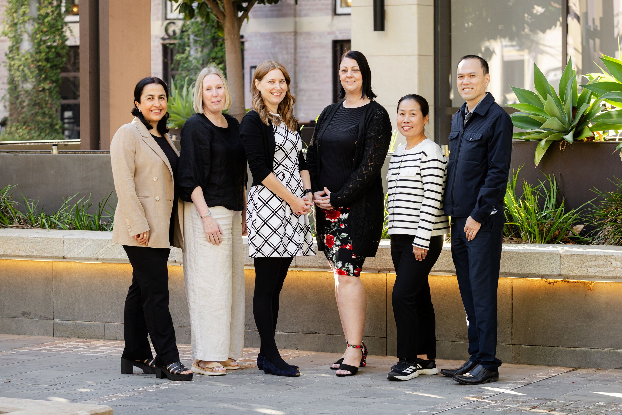 Six diverse business professionals stand together in front of a modern office building.