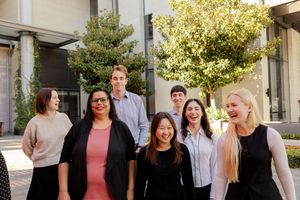 A diverse group of professionals smile together during an outdoor photo session on a sunny day.