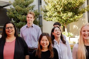 A cheerful group of professionals smiling together outdoors on a sunny day with trees in the background.