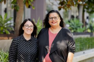 Two professional women wearing glasses pose together in front of a garden setting.