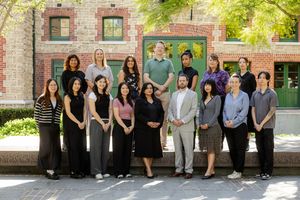 Group of professionals lined up against a brick building exterior for a team photo.