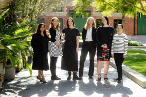 Professional team photo with people standing in front of a brick building entrance in sunlight.