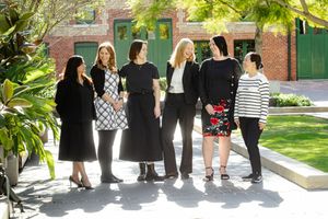 Group of six professionals standing together in casual business attire against a lush garden backdrop.
