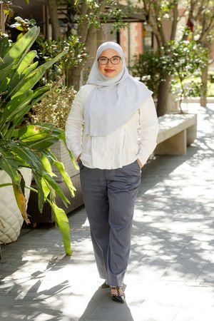Woman in white modest fashion outfit and hijab poses against sunny outdoor garden backdrop.