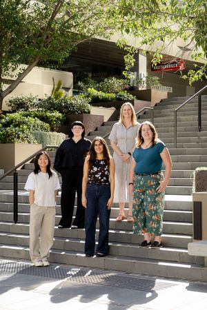 Professional team posing on concrete steps with trees and greenery in the background.