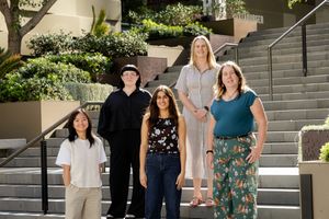 A diverse group stands together on outdoor steps with landscaping and modern architecture visible.