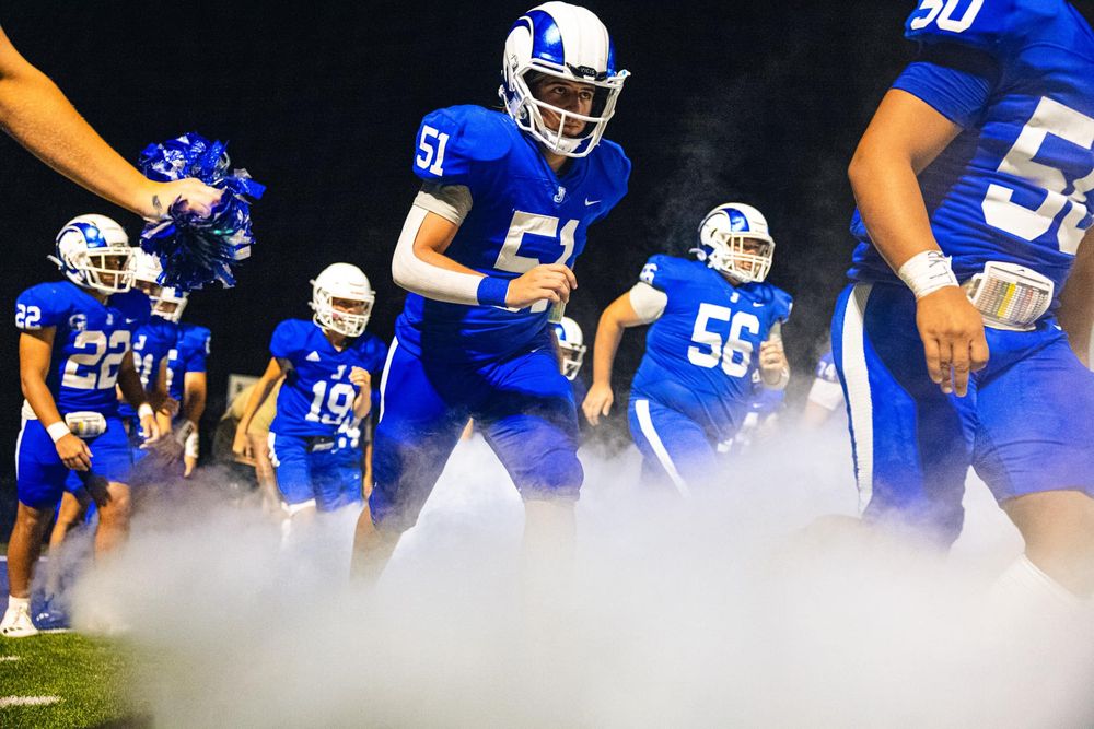 Football team line-up showing players in blue jerseys with white helmets on field at night.