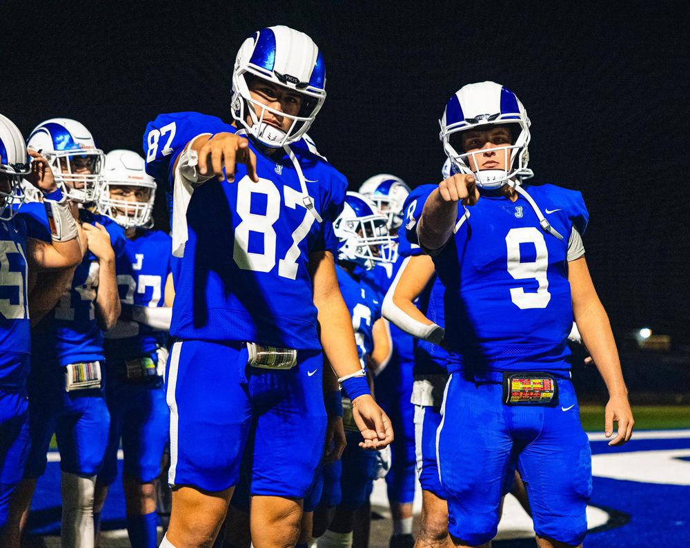 Football team in blue uniforms and white helmets preparing for play during night game.