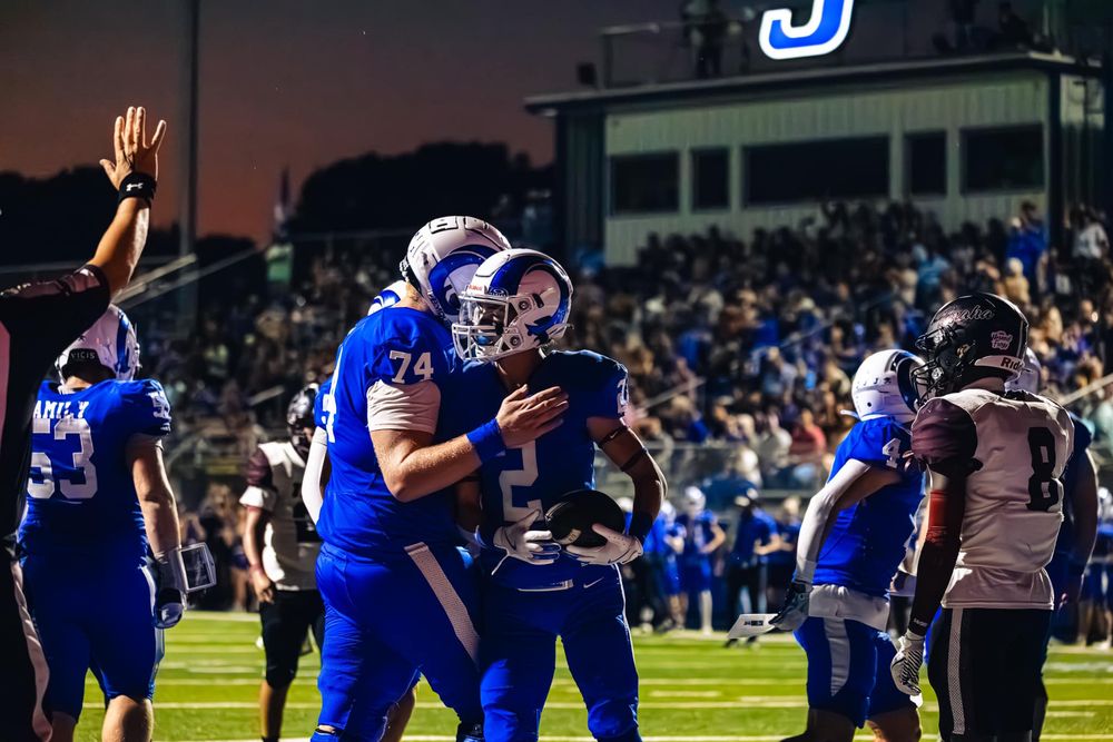 High school football team on sidelines during night game wearing blue and white uniforms.