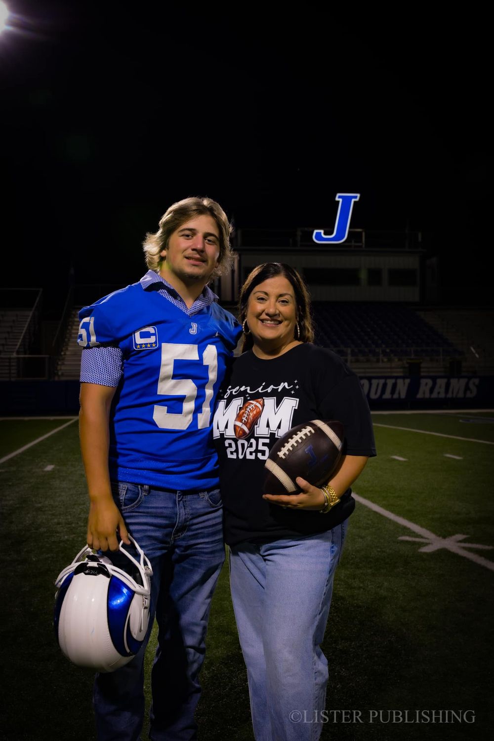 Football player and parent stand together on field holding commemorative football.
