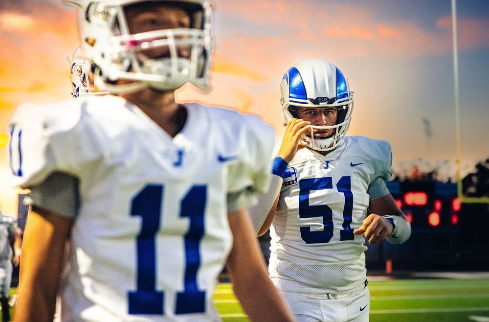 Football players in blue and white uniforms against sunset sky during evening game.