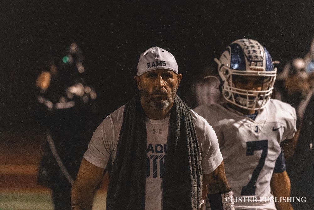 Coach and player stand on sideline during nighttime football game.