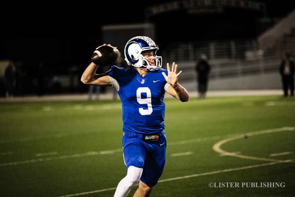 Football player in blue jersey taking position on dark field under stadium lights.