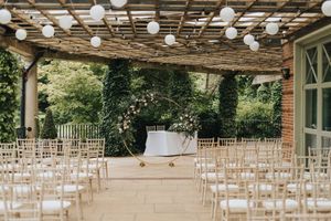 Rows of white folding chairs are set up under a wooden pergola for an outdoor wedding ceremony.