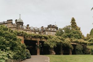 Historic stone building with ivy-covered walls and domed architecture set against a cloudy sky in an English garden setting.