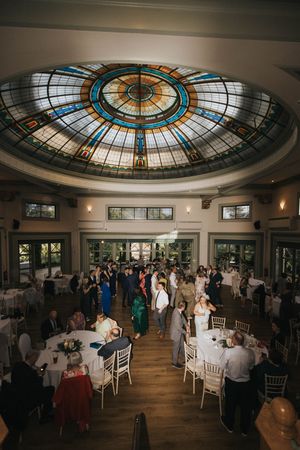 Wedding reception under a stunning stained glass dome ceiling in an elegant ballroom with white tables and chairs.