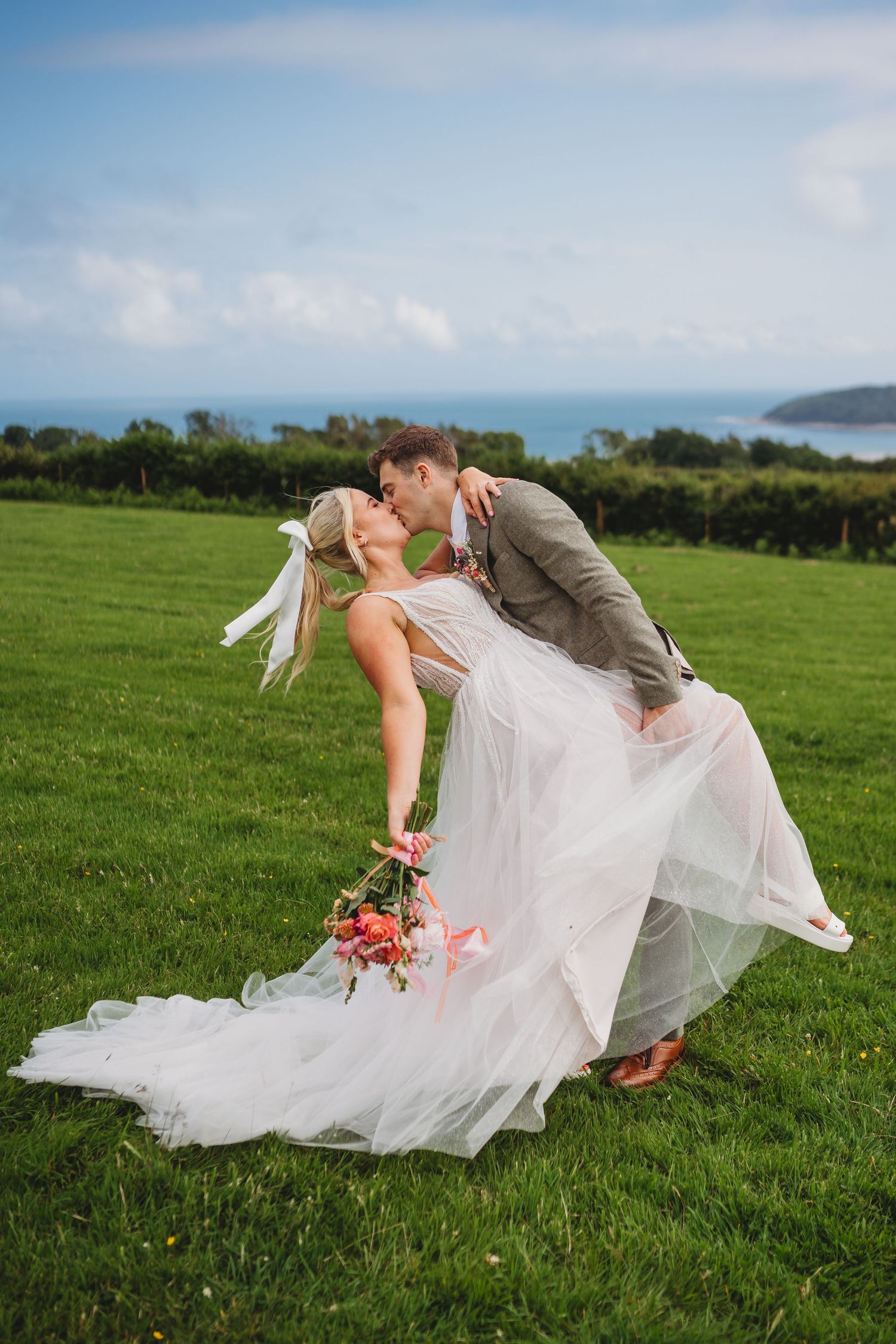A romantic wedding dip pose captured in a green field with blue skies.