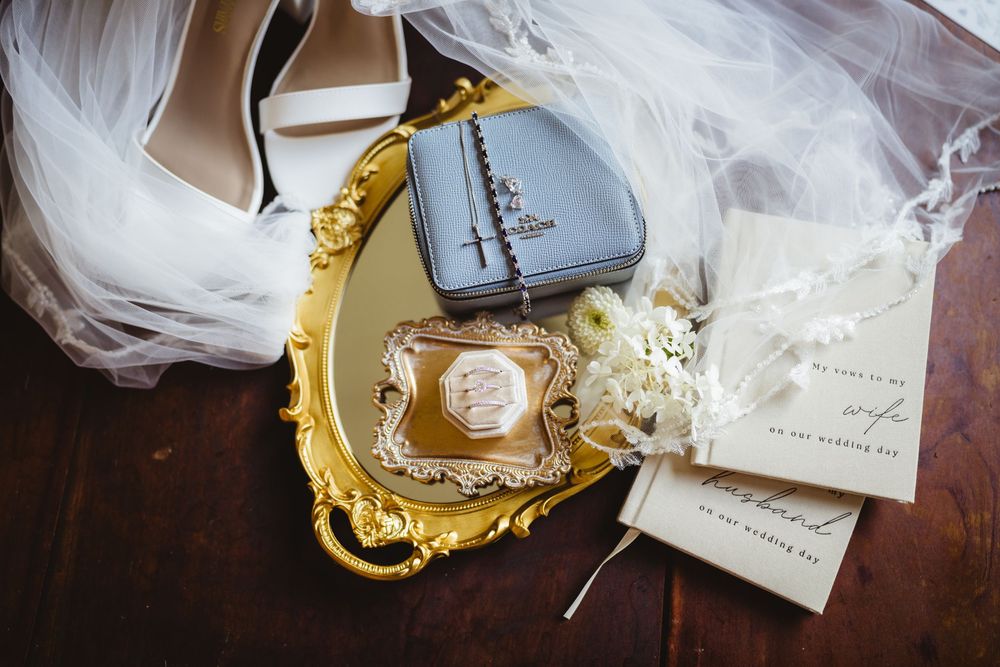 Elegant wedding details including perfume bottle and invitation placed on ornate gold tray with white tulle accents.