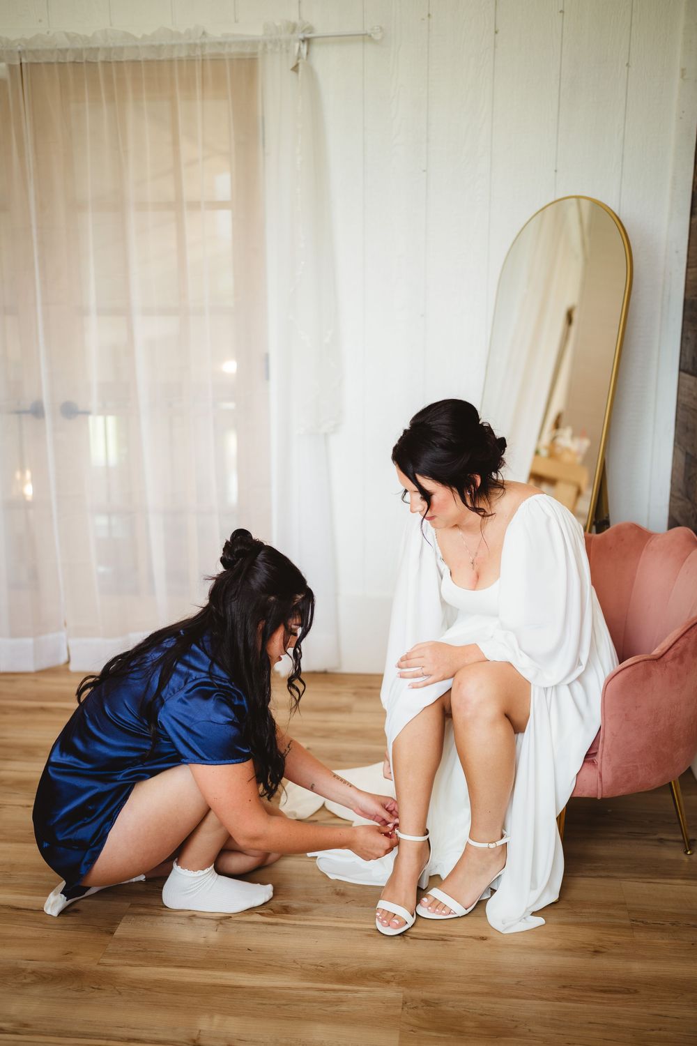 Getting ready scene with two women in white and blue robes preparing for a special occasion in a bright room.