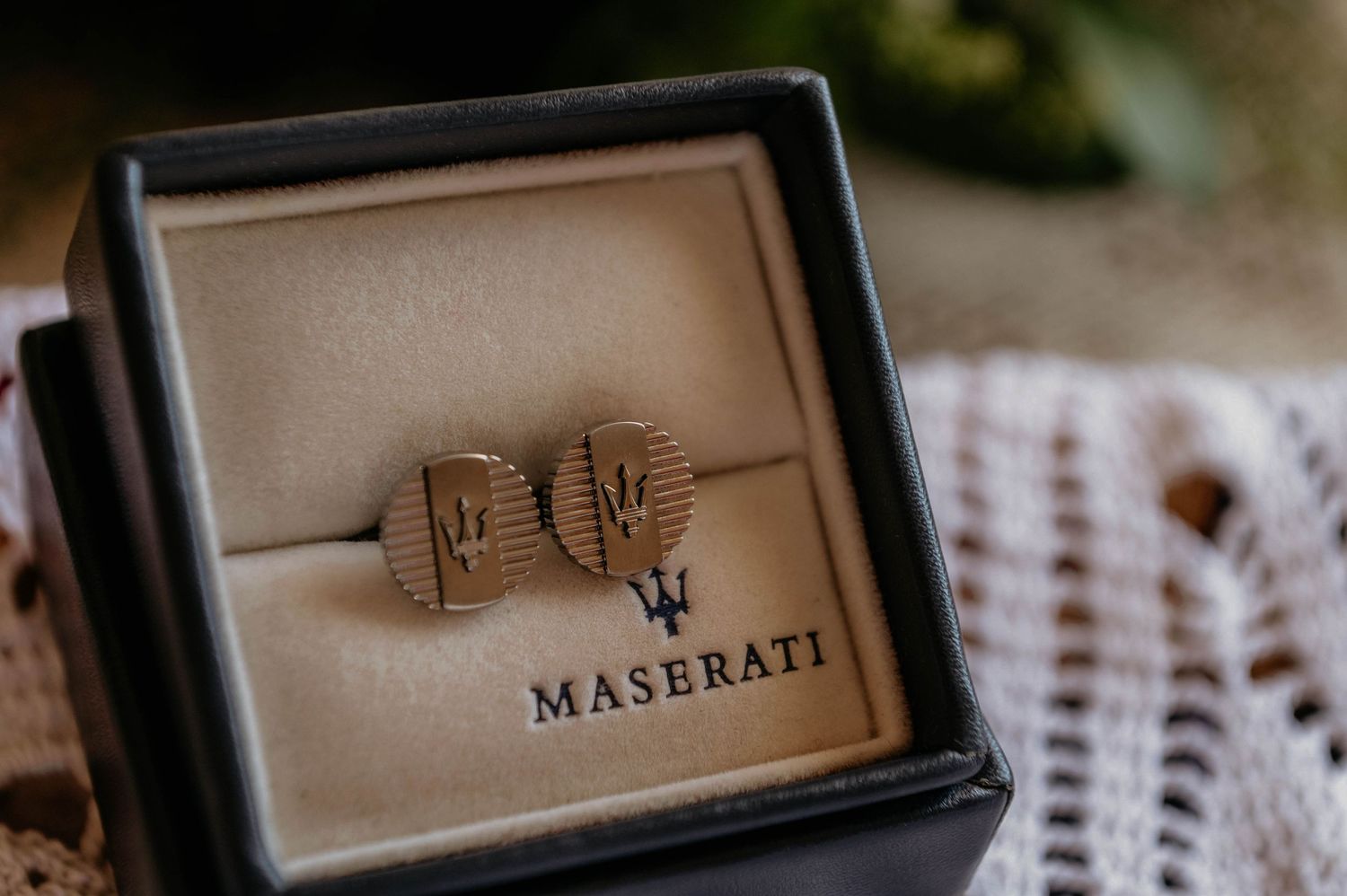 Two rose gold wedding bands sit in a black Maserati jewelry box on a textured surface.