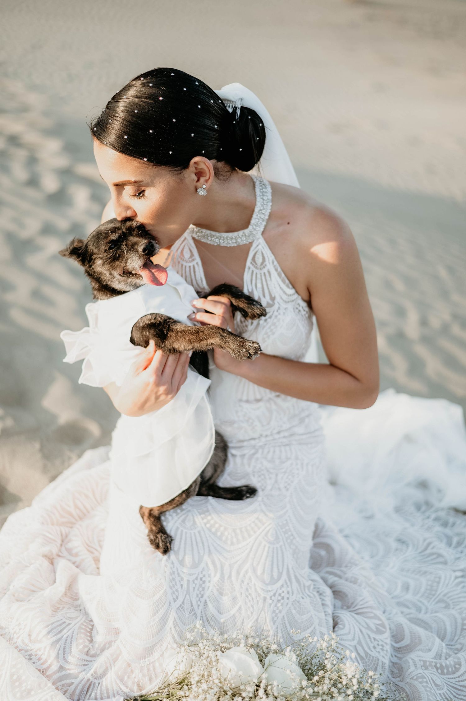 White lace wedding dress elegantly spread on sandy beach with decorative floral bouquet and soft lighting at golden hour.