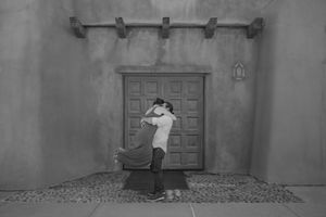 A black and white film frame showing a person emerging through a doorway in a dramatic scene. New Mexico queer wedding photographer.