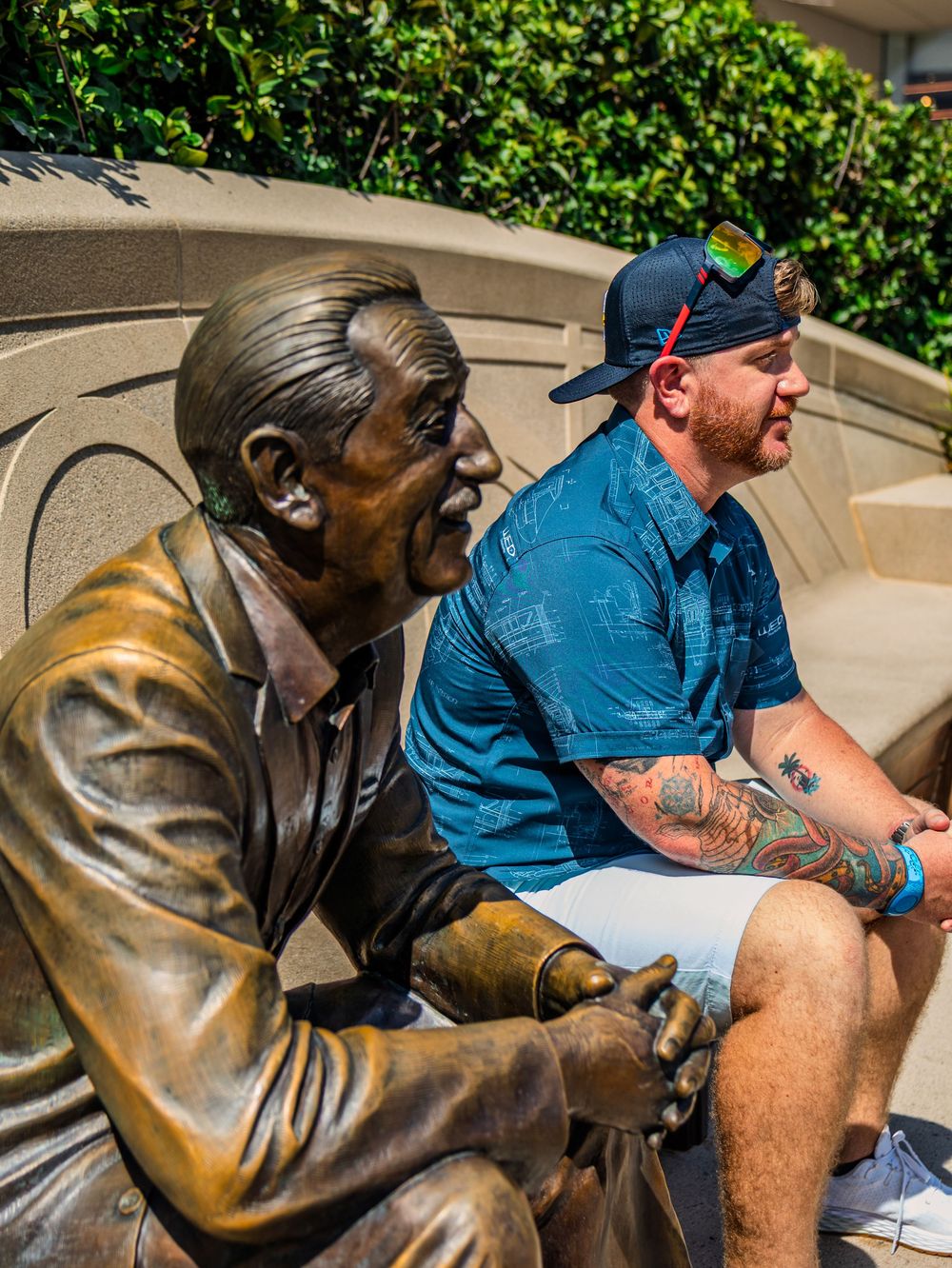 Close-up of person sitting beside detailed bronze statue on stone bench.