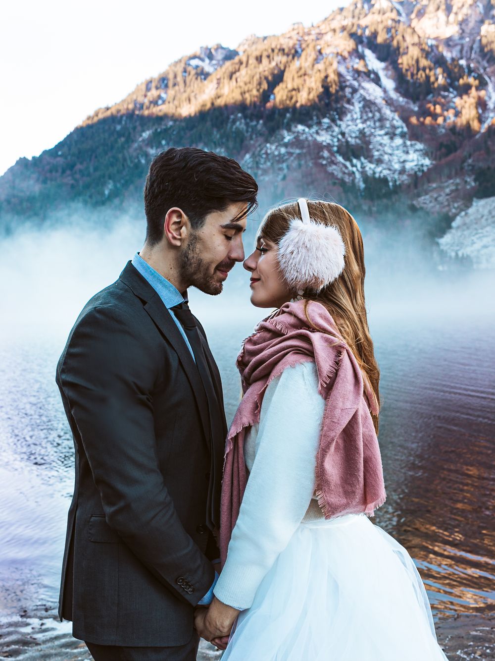 A romantic couple shares tender moments by a misty mountain lake during a winter wedding photoshoot.