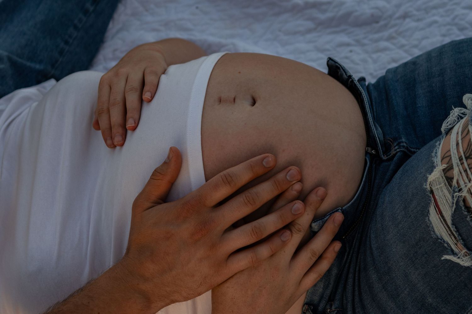 A young expecting couple has their hands on the mother's stomach.