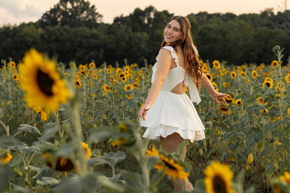 A figure in a white dress twirls through a vibrant sunflower field during golden hour.
