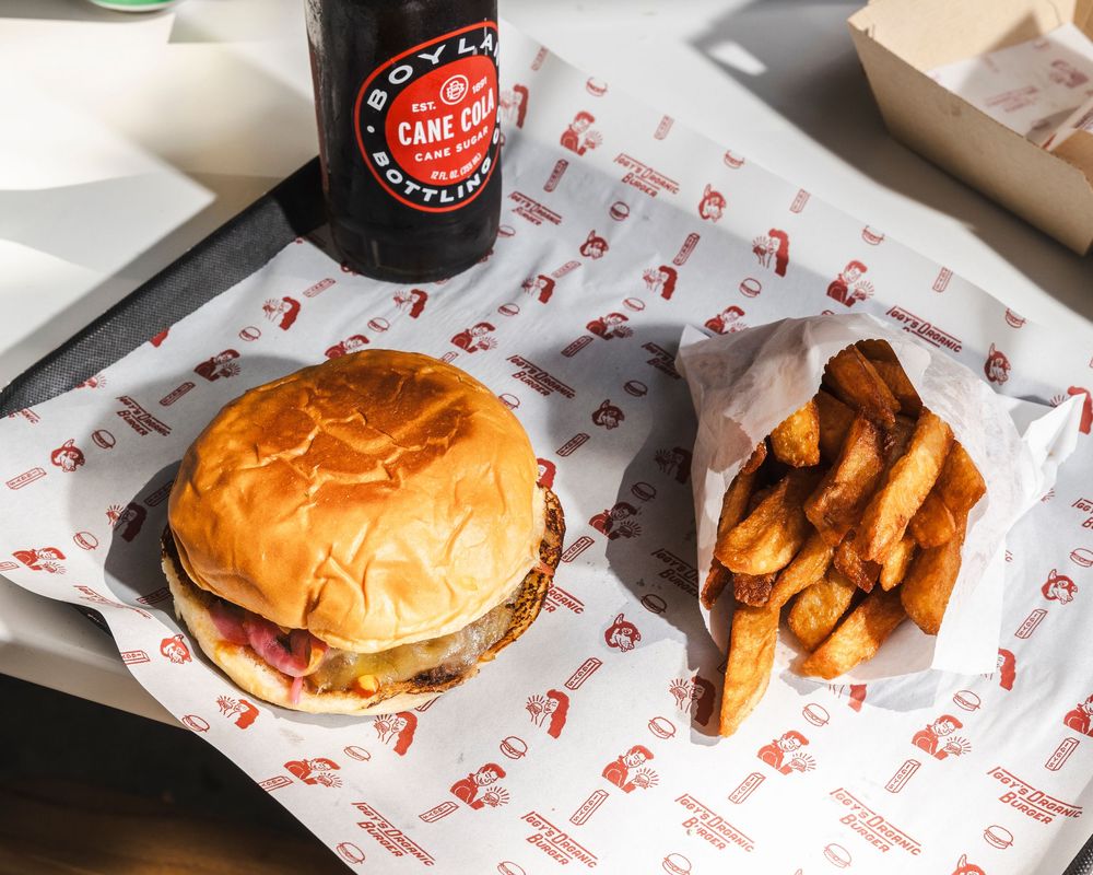A cheeseburger and french fries served on branded paper wrapper with a dark beverage bottle in the background.