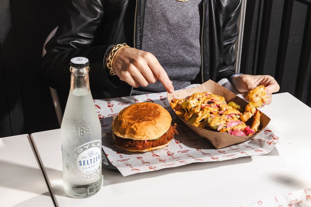 A casual dining scene with a burger, fries and clear glass bottle of soda on a marble table with paper liners.