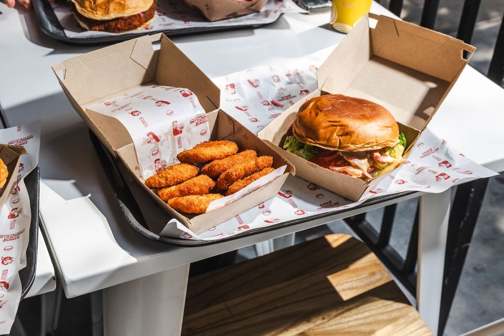Fast food takeout boxes and containers with burgers and chicken wings displayed on a dark surface.