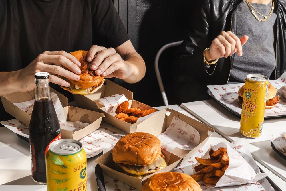 People enjoying gourmet burgers and beverages at a modern restaurant table with natural lighting.