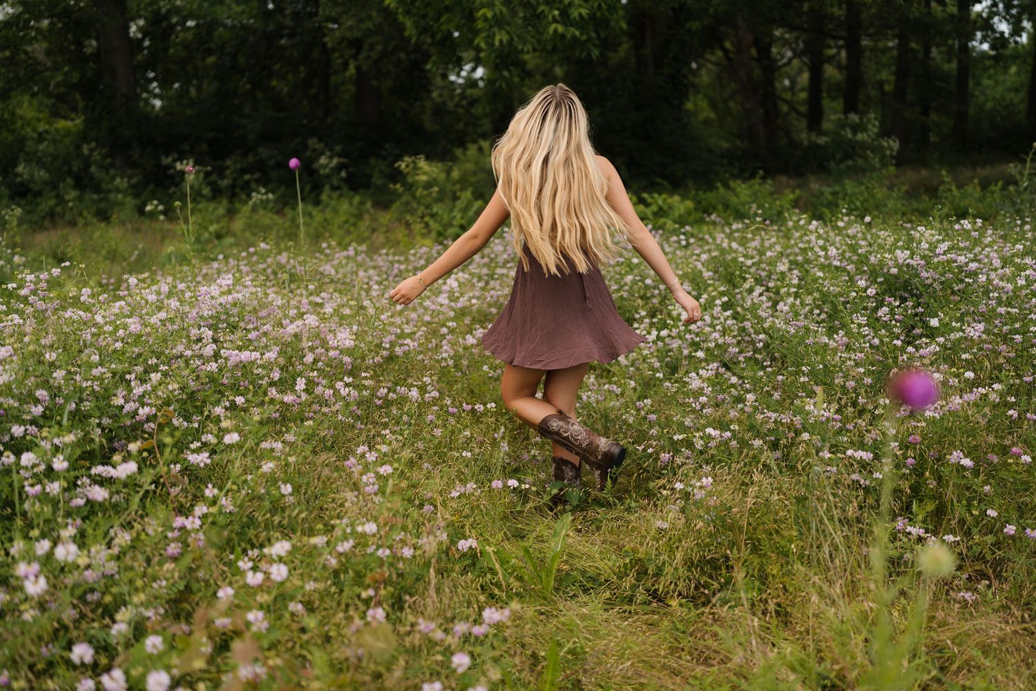 Someone with flowing blonde hair twirls through a meadow filled with pink and white wildflowers on a summer day.