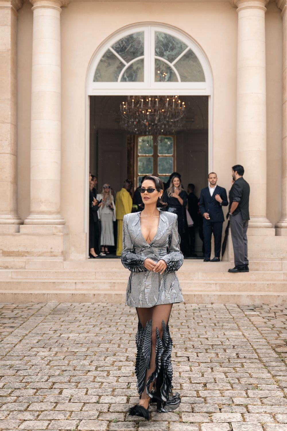 Fashionable outfit featuring silver blazer and patterned dress photographed at elegant venue with stone columns.