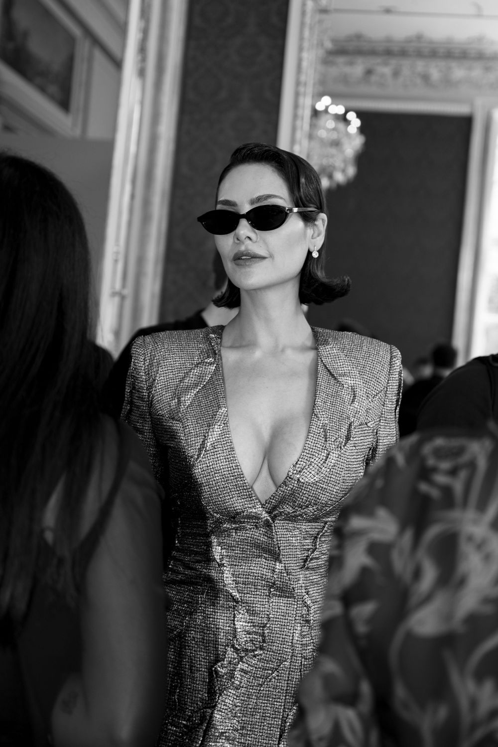 Model in metallic silver blazer and sunglasses poses dramatically at formal indoor event.