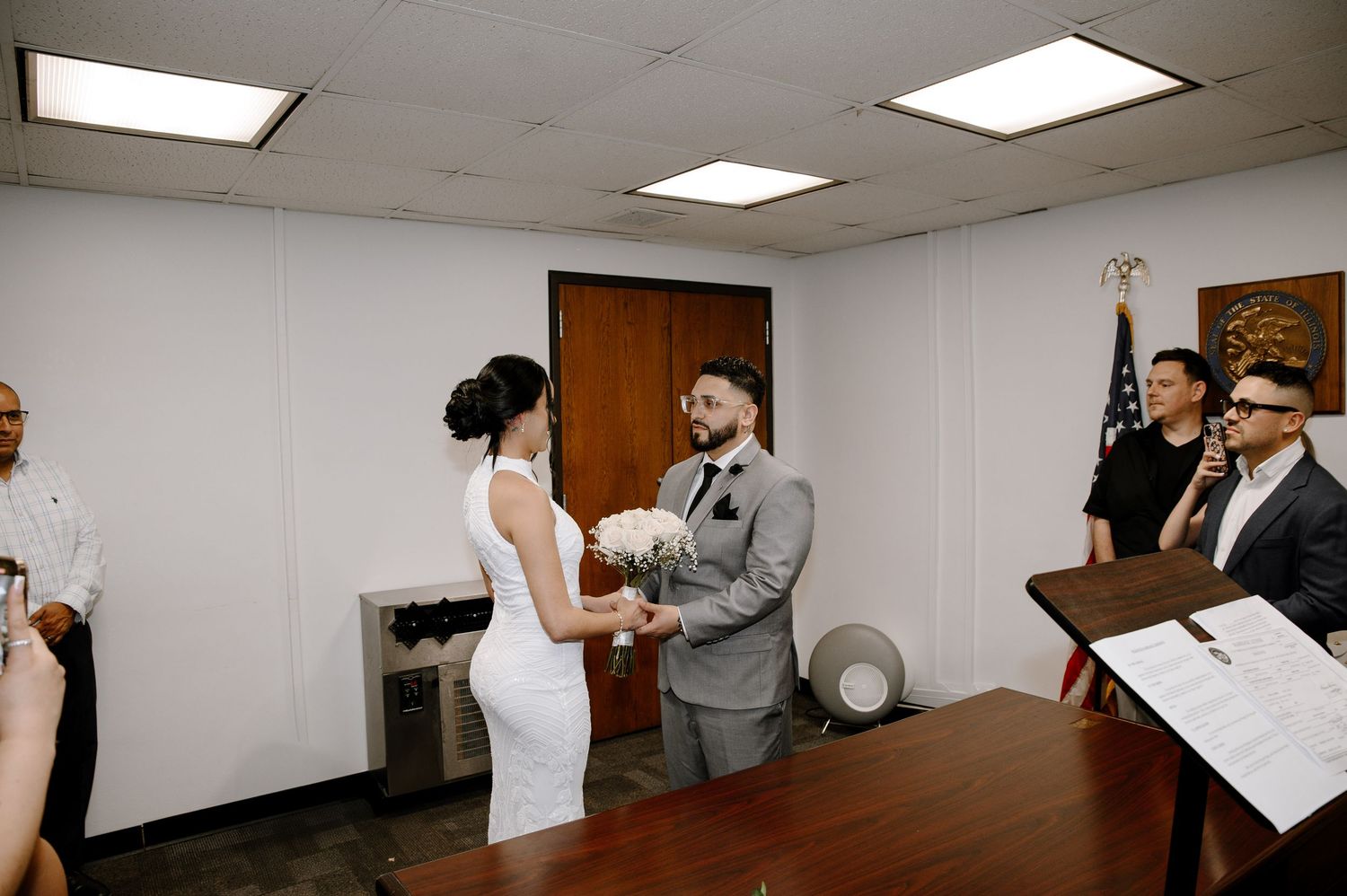 Modern indoor wedding ceremony with couple exchanging rings at courthouse while witnesses look on.
